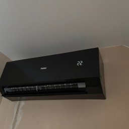 OPTIMAL-PLAST Rafał Pajdak - Czarna klimatyzacja Haier na ścianie w jasnym pomieszczeniu, widoczny wyświetlacz z temperaturą 22 stopnie. Świeżo pomalowana ściana.