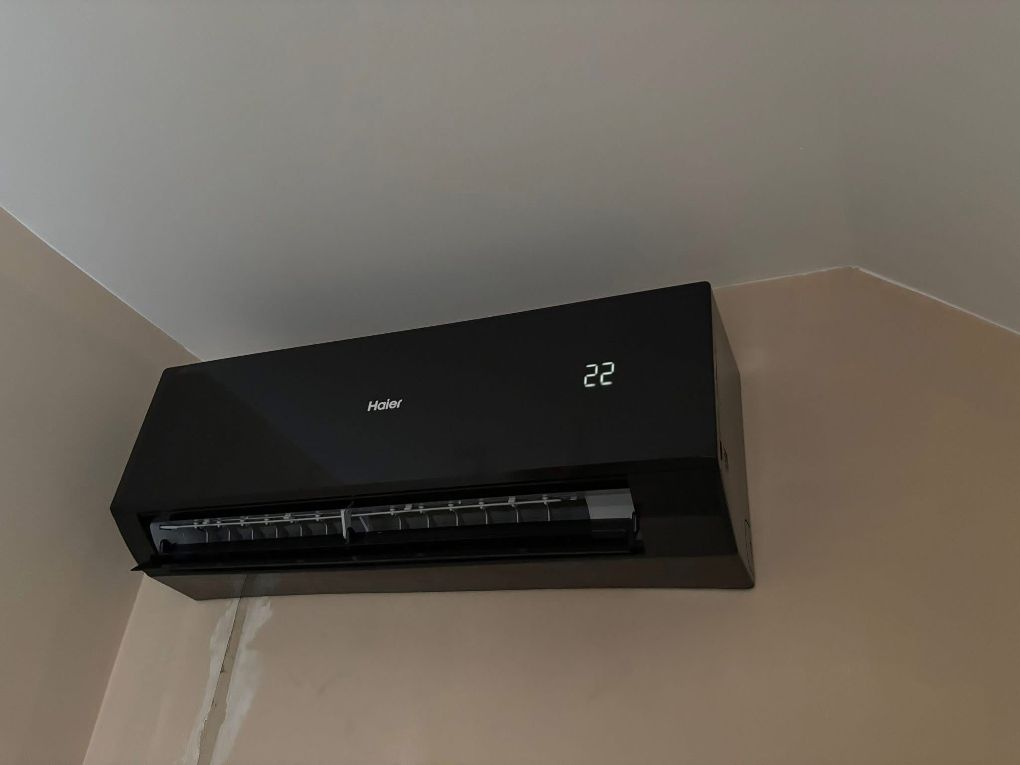 Czarna klimatyzacja Haier na ścianie w jasnym pomieszczeniu, widoczny wyświetlacz z temperaturą 22 stopnie. Świeżo pomalowana ściana.