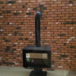 Ciemny piec wolnostojący z czarną rurą dymową na tle ściany wyłożonej dekoracyjną cegłą imitującą starą czerwoną cegłę z ciemnymi przebarwieniami, podświetlonej listwą LED.