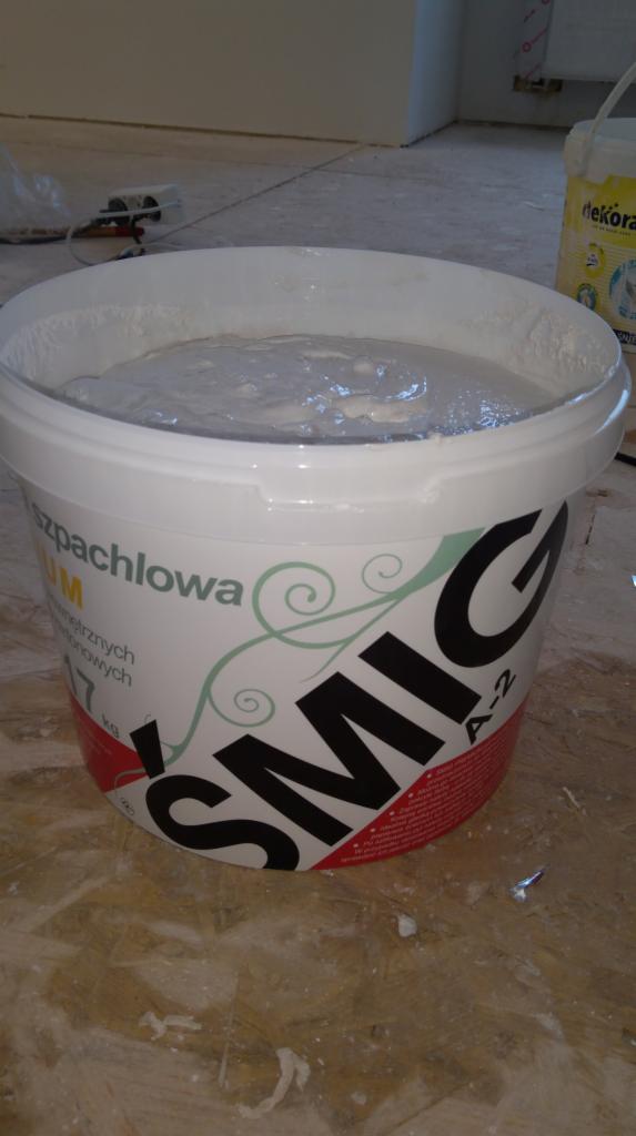 Wiadro ze świeżo wymieszaną masą szpachlową marki Śmig A-2, stojące na podłodze w trakcie prac wykończeniowych.
