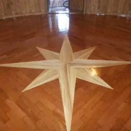 Parkiet ułożony w jodełkę z centralnie umieszczoną, jasną gwiazdą z drewna, widok z góry, polakierowana powierzchnia.