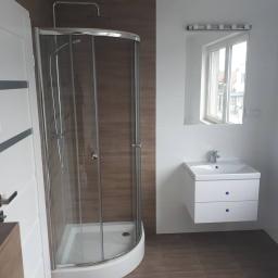 Group Service PL - Nowoczesna łazienka po remoncie z kabiną prysznicową z chromowanymi elementami, białą szafką pod umywalkę z dwoma szufladami i dużym lustrem z oświetleniem punktowym.