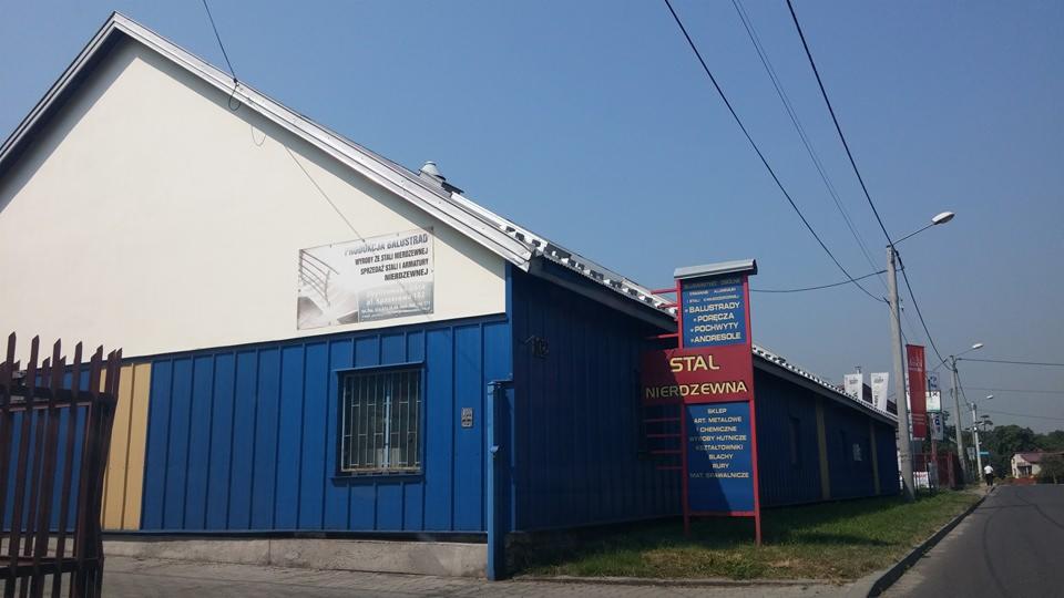 Budynek firmy zajmującej się obróbką stali nierdzewnej, z widocznymi tablicami reklamowymi oferowanych usług, takich jak balustrady i poręcze.