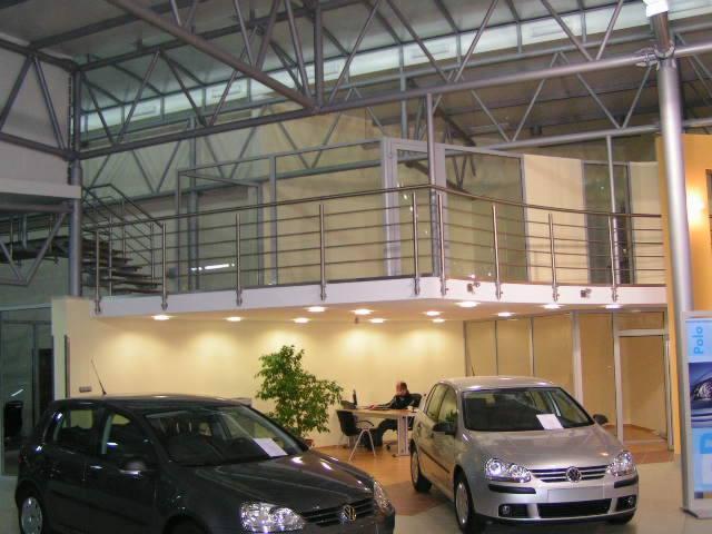 Metalowa konstrukcja antresoli z balustradą ze stali nierdzewnej w salonie samochodowym, widoczne dwa samochody marki Volkswagen Golf.