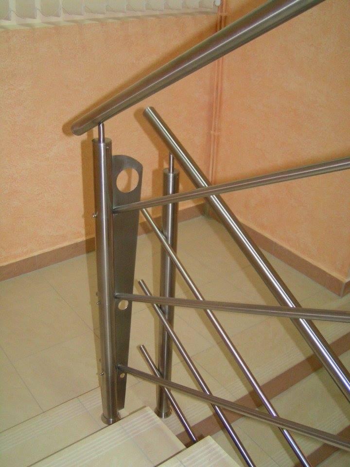 Szczegółowe ujęcie nowoczesnej, metalowej balustrady schodowej z elementami dekoracyjnymi w kształcie łezki i ukośnymi prętami, zamontowanej na stopniach wyłożonych płytkami.