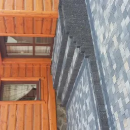 Elewacja domu z drewnianą boazerią i fragmentem ściany wykończonej kostką w odcieniach szarości, widok z dołu.