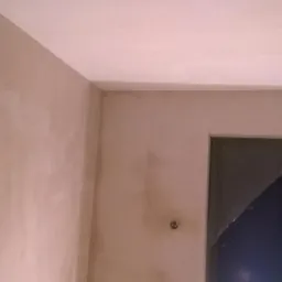 Ściana i sufit po nałożeniu gładzi, widoczne niedoskonałości i pozostałości po instalacji elektrycznej na suficie, przygotowane do dalszych prac wykończeniowych.