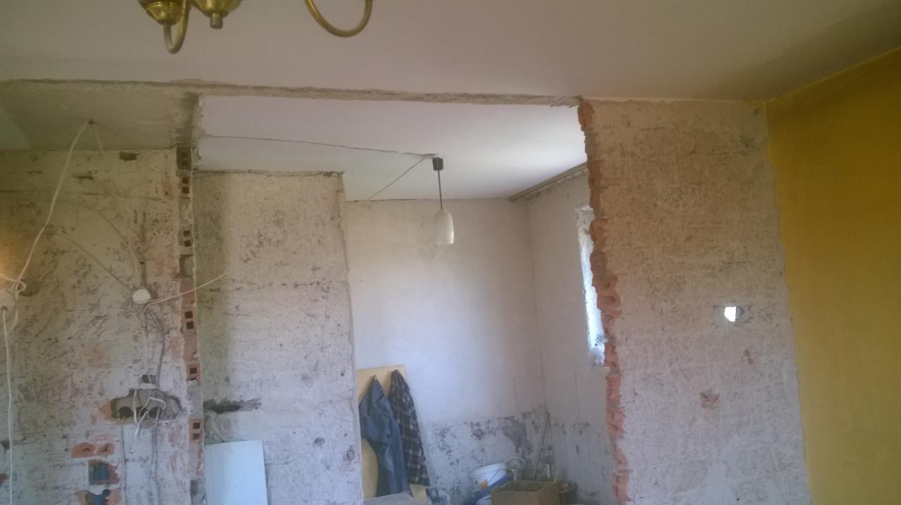 Wnętrze w trakcie remontu: odsłonięta cegła, fragmenty starej farby, wisząca lampa, widoczne przewody elektryczne, przygotowanie do dalszych prac wykończeniowych.