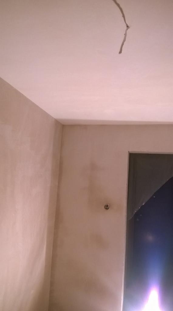 Ściana i sufit po nałożeniu gładzi, widoczne niedoskonałości i pozostałości po instalacji elektrycznej na suficie, przygotowane do dalszych prac wykończeniowych.