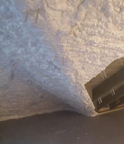 Poddasze z widoczną izolacją natryskową z pianki poliuretanowej, z metalowymi elementami mocującymi wystającymi z nierównomiernej powierzchni piany.