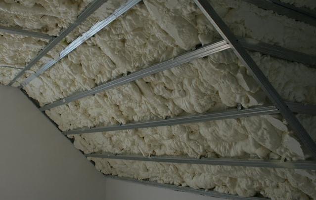 Poddasze z widoczną konstrukcją metalową, wypełnione spienionym materiałem izolacyjnym o nieregularnej strukturze.