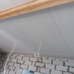 twoj nowy dom (osoba prywatna) - Płyty gipsowo-kartonowe na suficie podwieszanym, widoczne drewniane belki konstrukcyjne i wystające przewody elektryczne, ściana z białego bloczka w tle.