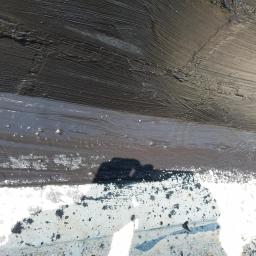 twoj nowy dom (osoba prywatna) - Świeżo nałożona, gruba warstwa czarnej hydroizolacji na dachu, z widocznymi śladami pędzla i odbiciem sylwetki osoby w mokrej powierzchni.