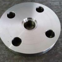 Okrągły, metalowy kołnierz z czterema otworami montażowymi i centralnym otworem, widoczny na szarym, lekko rozmytym tle.