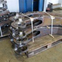 Surowe, stalowe elementy konstrukcyjne hali, połączone tymczasowo drewnianymi rozpórkami, ułożone na palecie przed montażem.