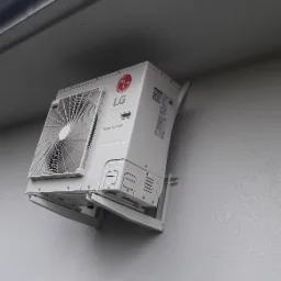 Zewnętrzna jednostka klimatyzacji LG Smart Inverter zamontowana na szarej ścianie budynku, widoczne rury i wsporniki montażowe.