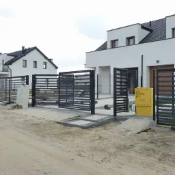 Rząd nowoczesnych domów jednorodzinnych z czarnymi, poziomymi ogrodzeniami panelowymi, widoczne skrzynki gazowe przy każdym domu.