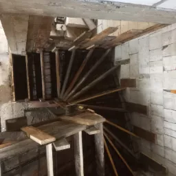 Szare betonowe schody w trakcie budowy z drewnianym szalunkiem i zbrojeniem stalowym, widok z góry w surowym pomieszczeniu z białymi ścianami z bloków.