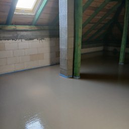 A&M Mariusz Batycki - Świeżo wylana, gładka wylewka anhydrytowa w pomieszczeniu na poddaszu z oknem dachowym. Widoczne drewniane elementy konstrukcyjne i ściany z bloczków.