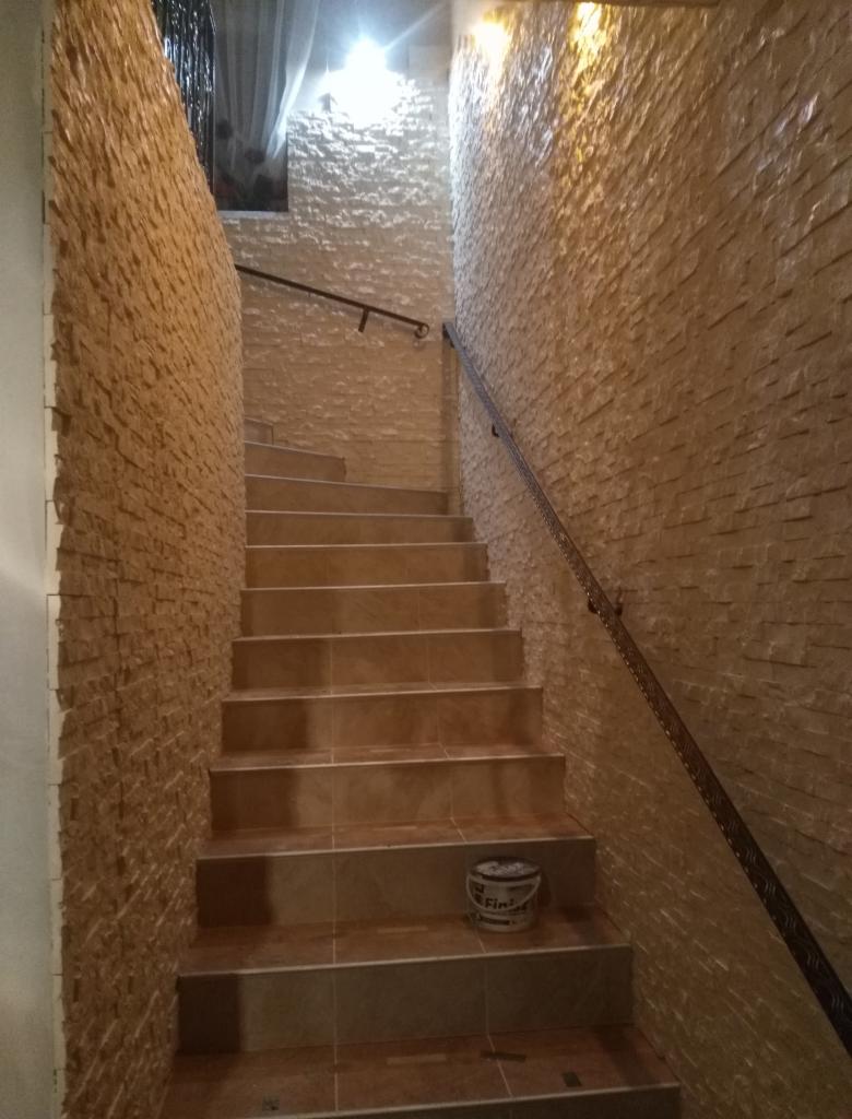 Schody wyłożone płytkami imitującymi kamień, z metalową poręczą, prowadzące w górę; na jednym ze stopni stoi puszka z farbą.