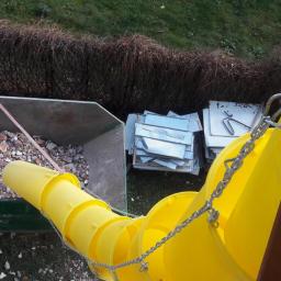 Dominik-KRAK-TRANS-BUD - Zielony kontener wypełniony gruzem budowlanym, obok stos blach, połączony z żółtą rurą zsypową z łańcuchem zabezpieczającym, widok z góry.