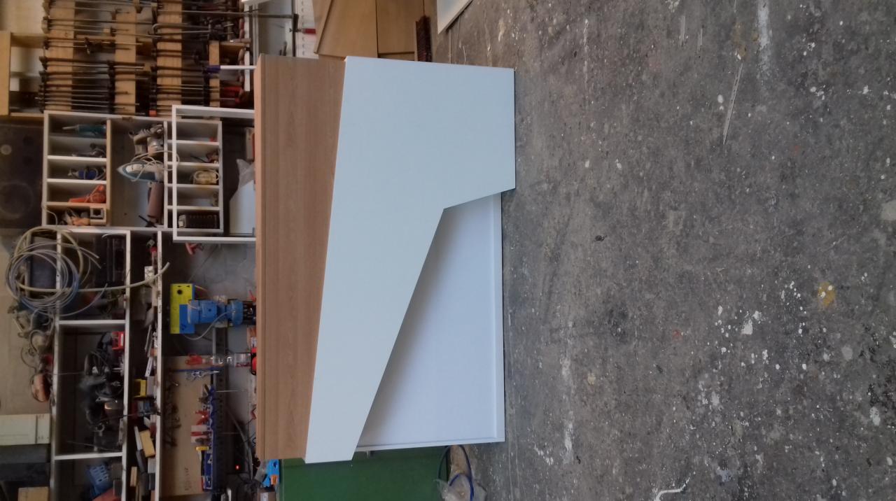 Element konstrukcyjny szafy z białymi frontami i korpusem z płyty drewnopodobnej, widoczny w warsztacie na tle regału z narzędziami.