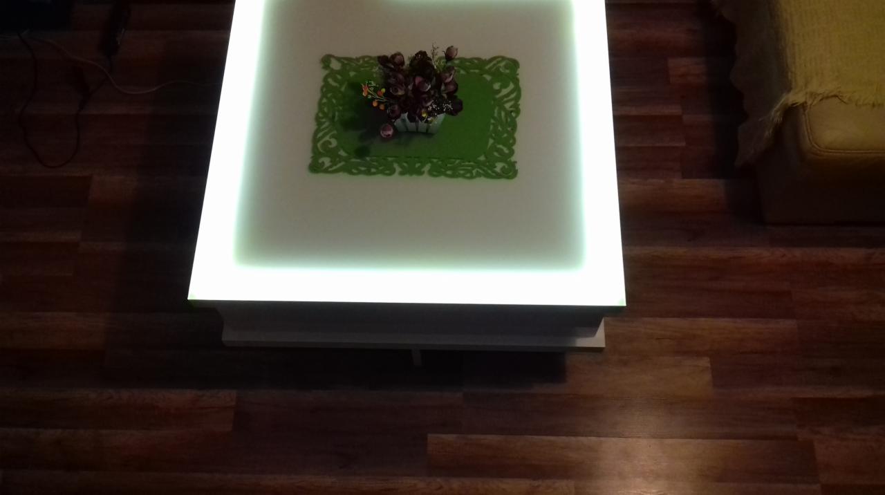 Podświetlany stolik kawowy z kwiatami, wykonany na wymiar w Banie, z blatem imitującym szafkę, stojący na drewnianej podłodze.