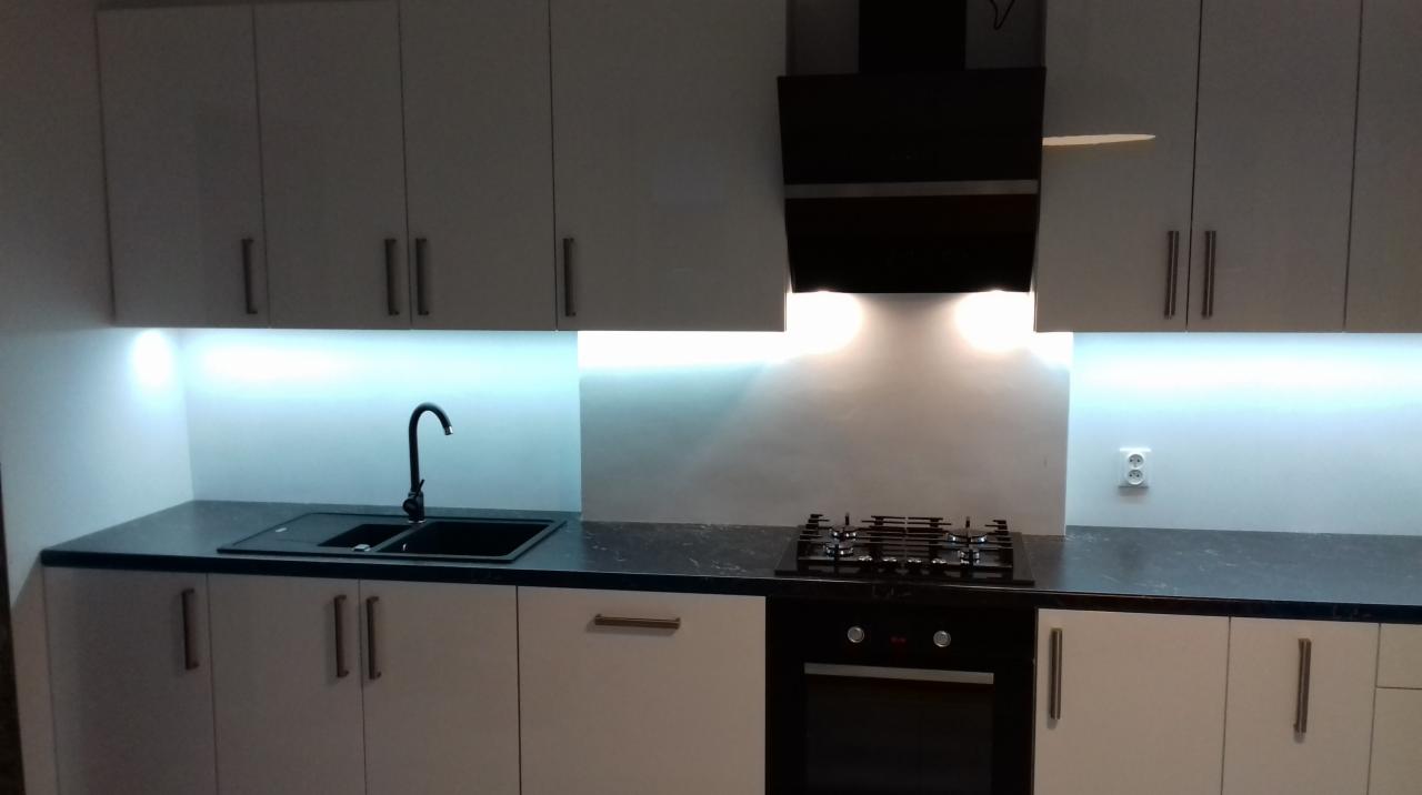 Nowoczesna kuchnia z białymi szafkami, czarnym blatem i czarną armaturą, oświetlenie LED pod szafkami górnymi.