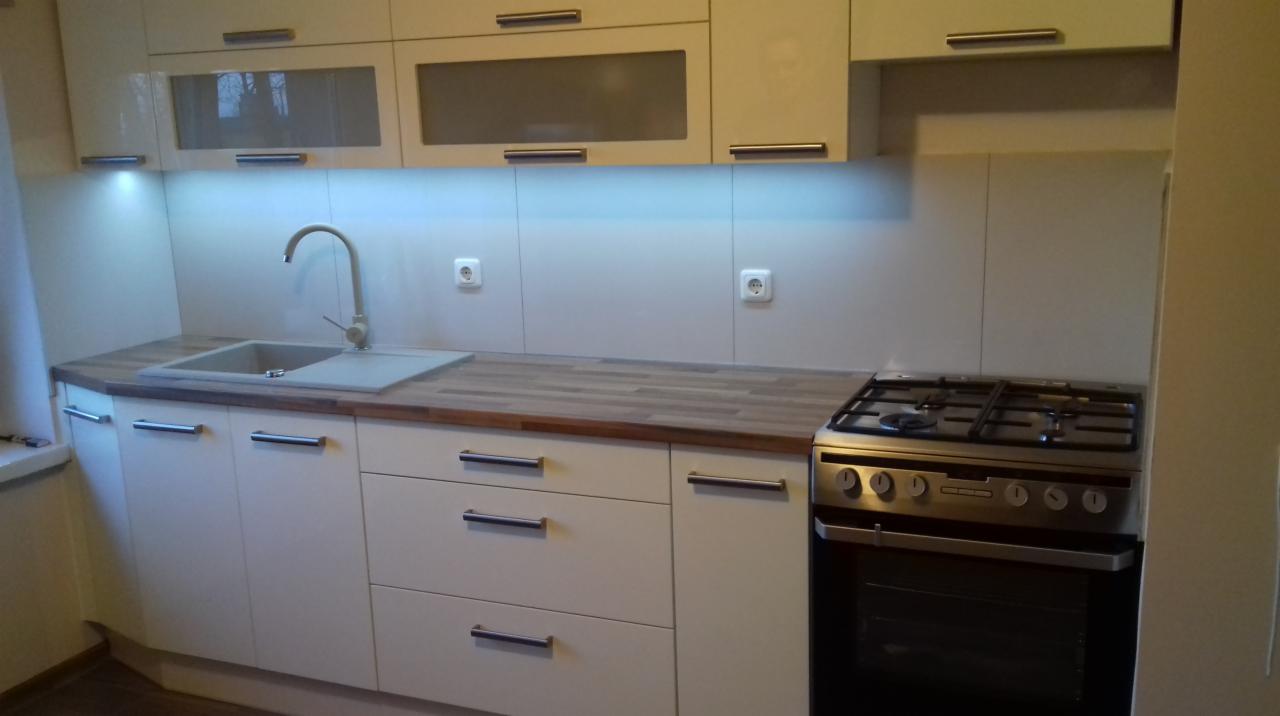 Jasna kuchnia z drewnianym blatem, zlewem i kuchenką gazową; górne szafki z przeszklonymi frontami, oświetlenie podszafkowe.