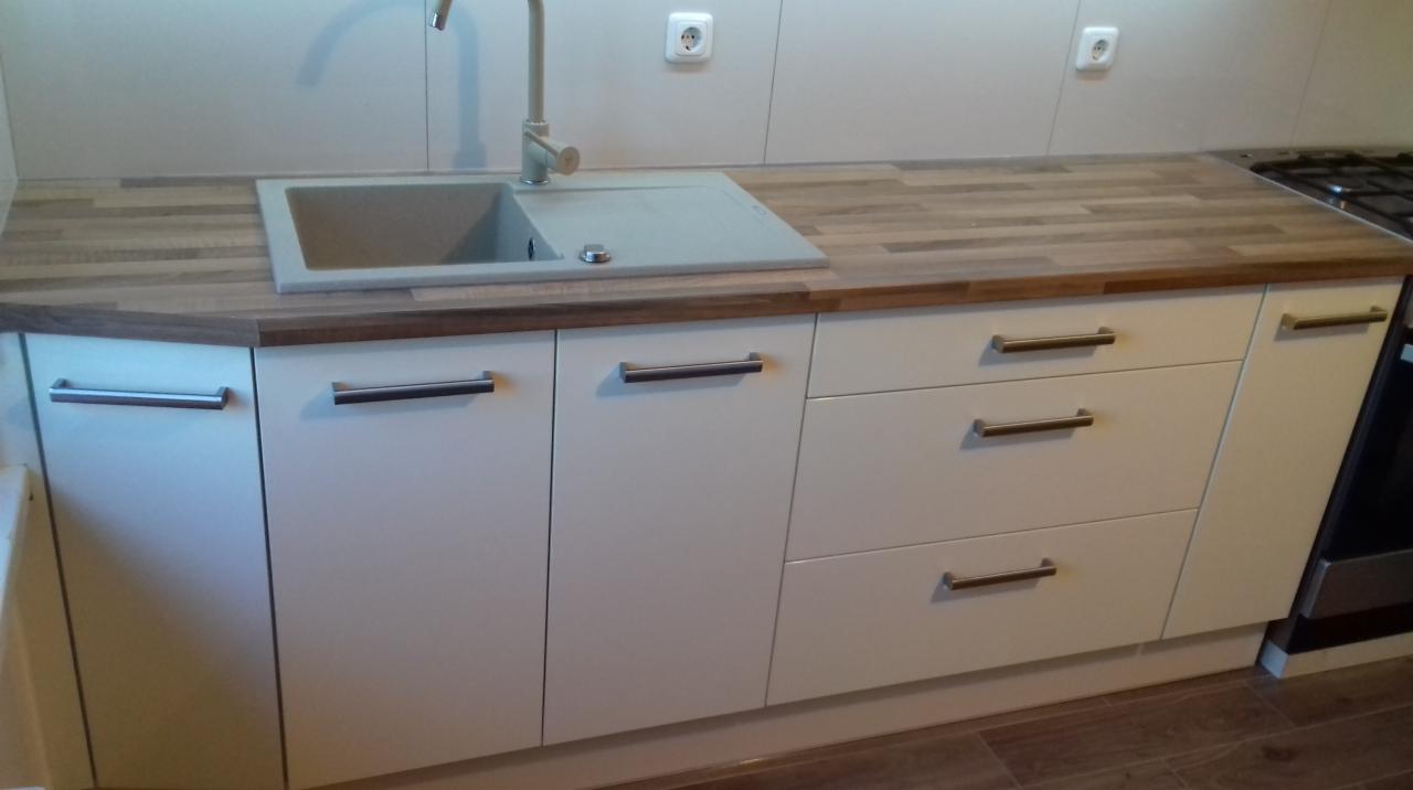 Białe szafki kuchenne z drewnianym blatem, szarym zlewem i baterią w nowoczesnej kuchni.