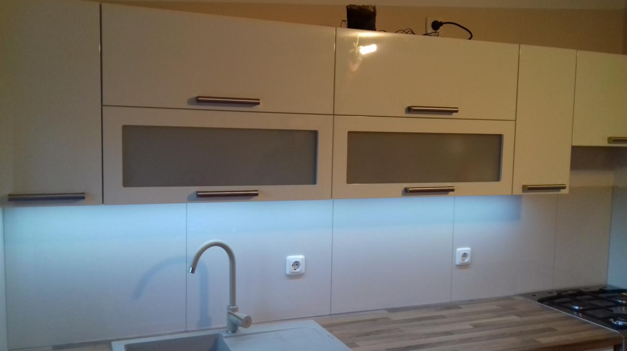 Białe szafki kuchenne na wymiar z podświetleniem LED pod szafkami, widoczny zlew i bateria.