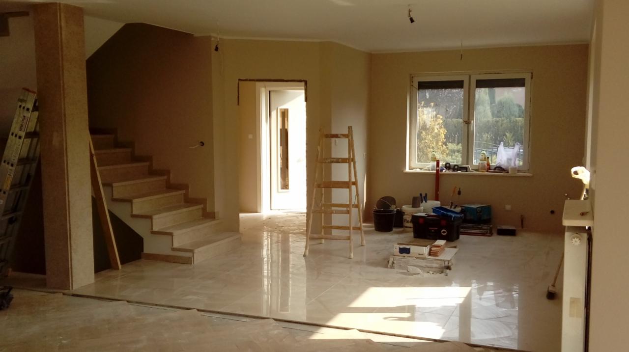 Wnętrze w trakcie remontu: świeżo pomalowane ściany w odcieniach beżu, marmurowe schody, podłoga z połyskiem, drabina malarska i akcesoria malarskie przy oknie.