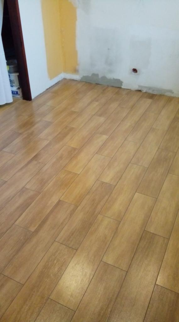 Ułożona podłoga z paneli imitujących drewno, ściana częściowo pomalowana na żółto, widoczne ślady po remoncie na ścianie i przy podłodze.