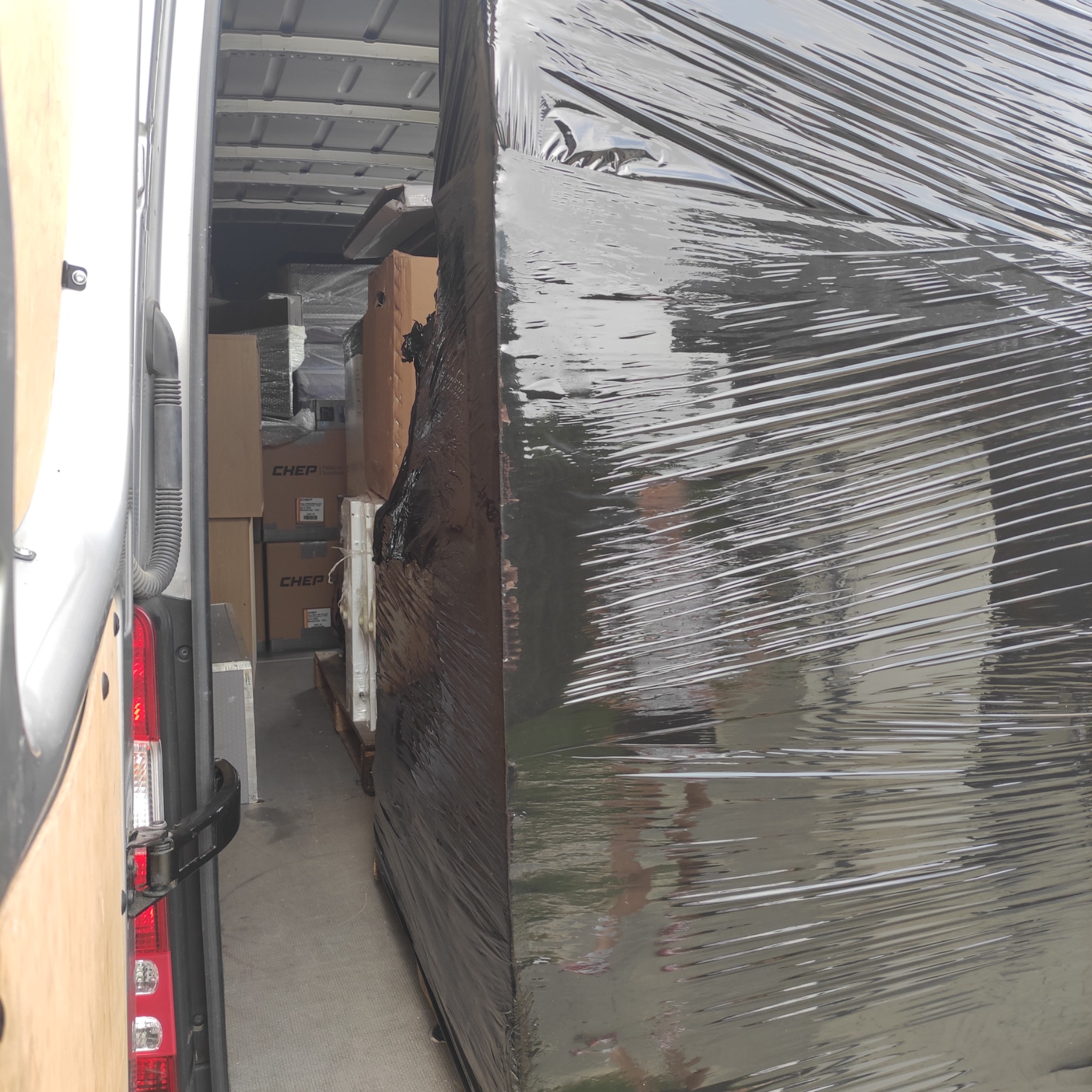 Wnętrze furgonetki załadowane kartonami i meblami owiniętymi folią stretch, widoczne skrzynie CHEP.