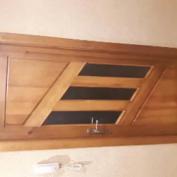 Drewniane drzwi wewnętrzne z trzema poziomymi szybami i ozdobnym wzorem, zamontowane w ścianie nad niskim kontaktem telefonicznym.