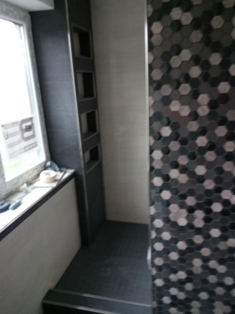 Wykończona łazienka z heksagonalną mozaiką na ścianie, wnękami obok okna i ciemną podłogą.