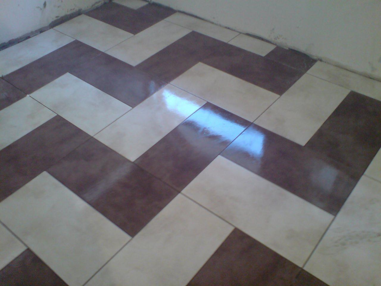 Ułożona wzór jodełki z brązowych i beżowych płytek podłogowych, widoczne odbicie światła na powierzchni płytek.