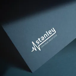 Eleganckie białe logo 'Stanley Centrum Medyczne' z elementem EKG na ciemnoniebieskim fakturowanym papierze, oświetlone z góry, leżące pod kątem.