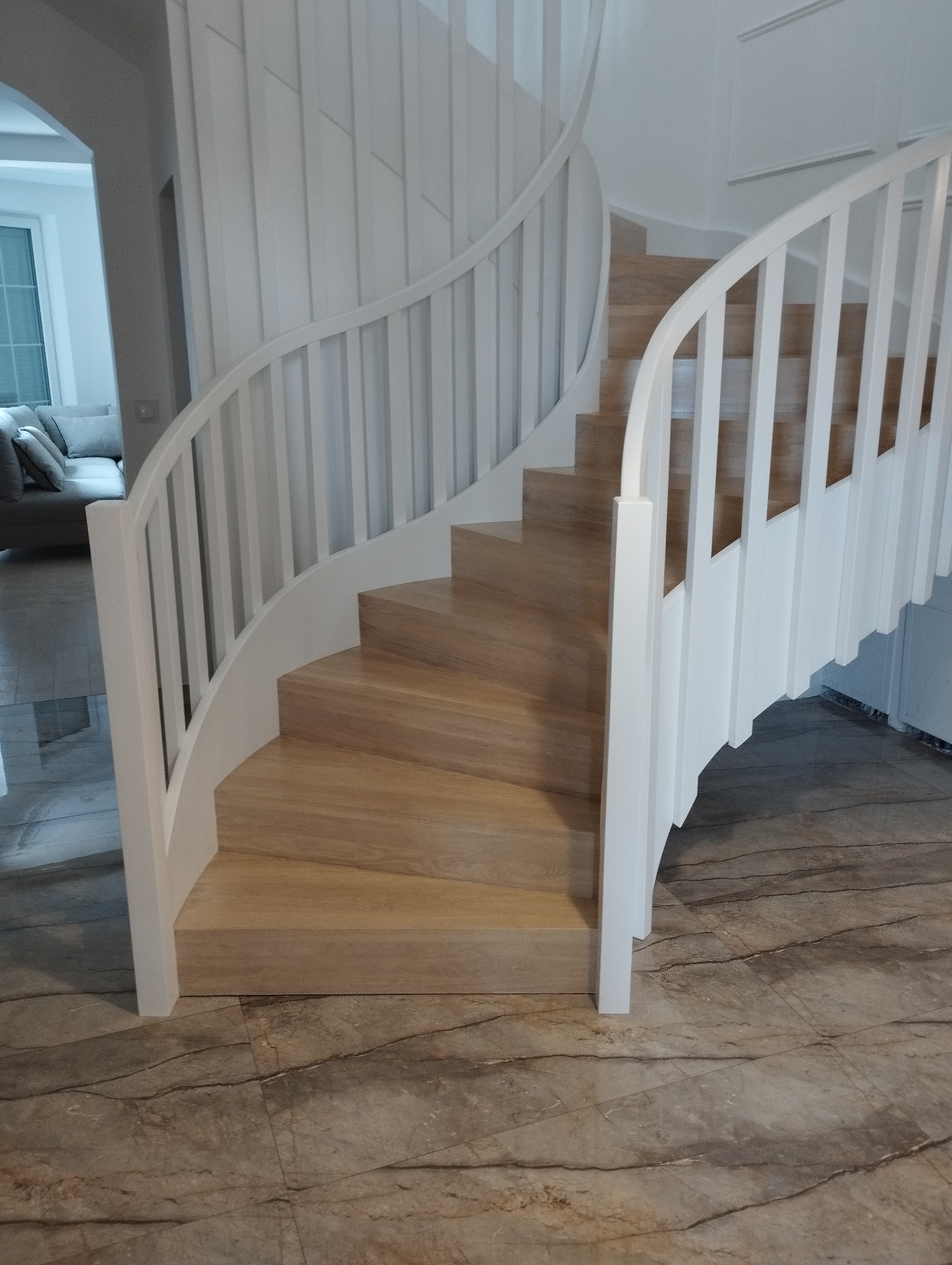 Spiralne schody z jasnego drewna i białymi balustradami, widok z dołu, marmurowa podłoga, nowoczesny design.
