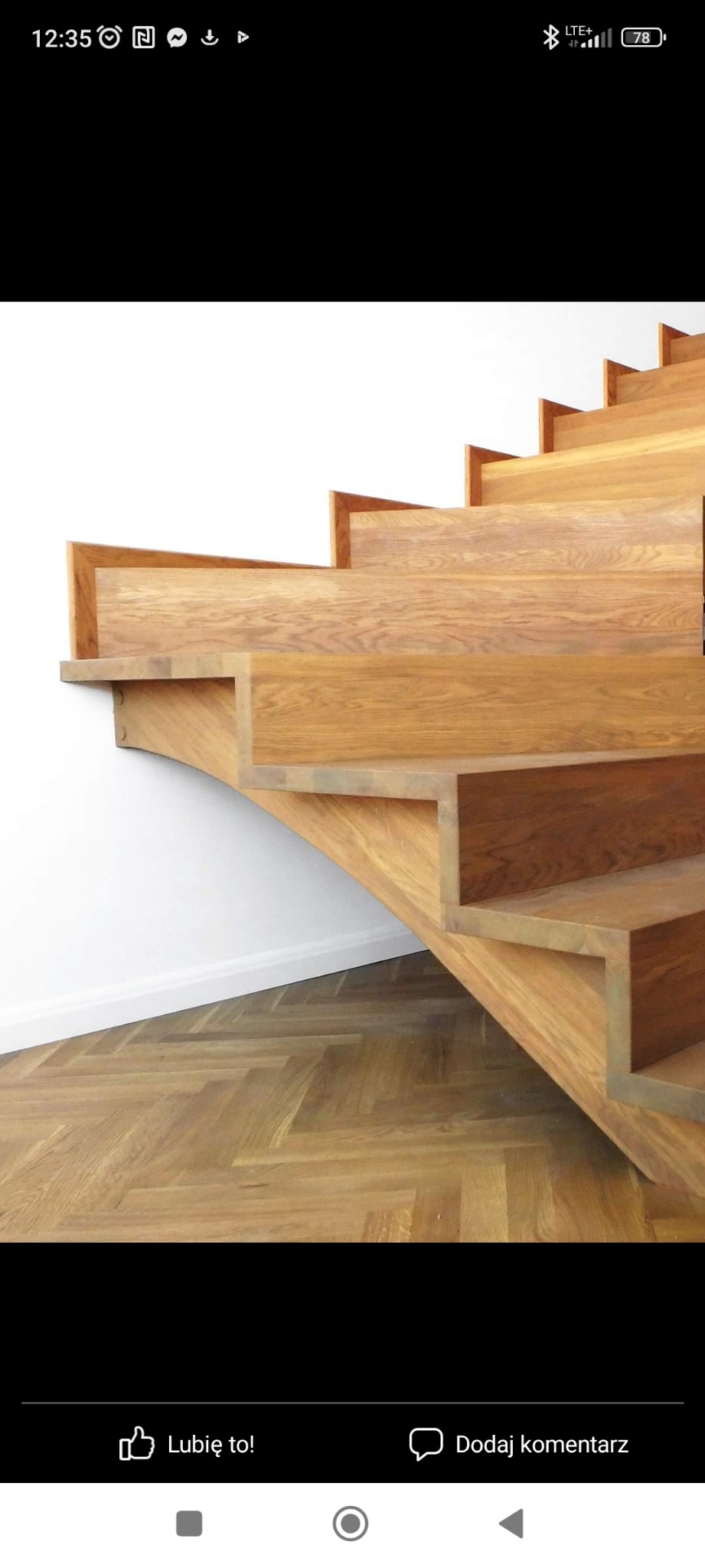 Drewniane schody o jasnym odcieniu drewna, z zakrętem, zamontowane przy białej ścianie i parkiecie ułożonym w jodełkę.