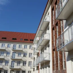 Dwa budynki wielorodzinne z balkonami o różnych konstrukcjach: jeden z balkonami ze schodami ewakuacyjnymi, drugi z prostymi, metalowymi barierkami