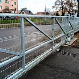 GERMAPLAN System Sp. z o.o. - Przesuwna brama z metalowej siatki panelowej z automatyką, widok z zewnątrz na tle chodnika i budynków.