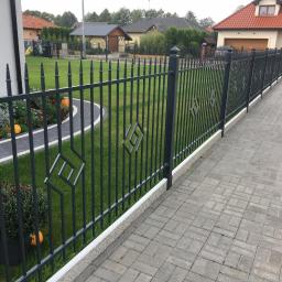 GERMAPLAN System Sp. z o.o. - Ciemnoszare, metalowe ogrodzenie z geometrycznym wzorem rombu, oddzielające posesję z trawnikiem i rabatami kwiatowymi od kostki brukowej podjazdu.