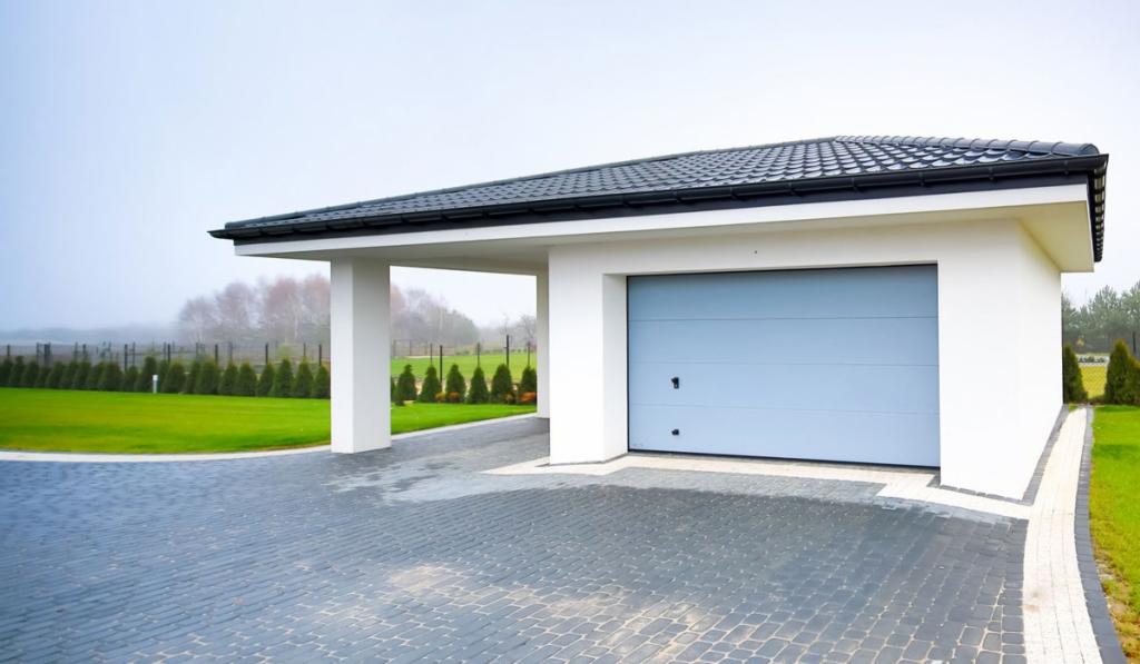 Nowoczesny garaż z szarą bramą segmentową, podjazd z kostki brukowej, minimalistyczna architektura budynku, zadbany trawnik z tujami w tle.