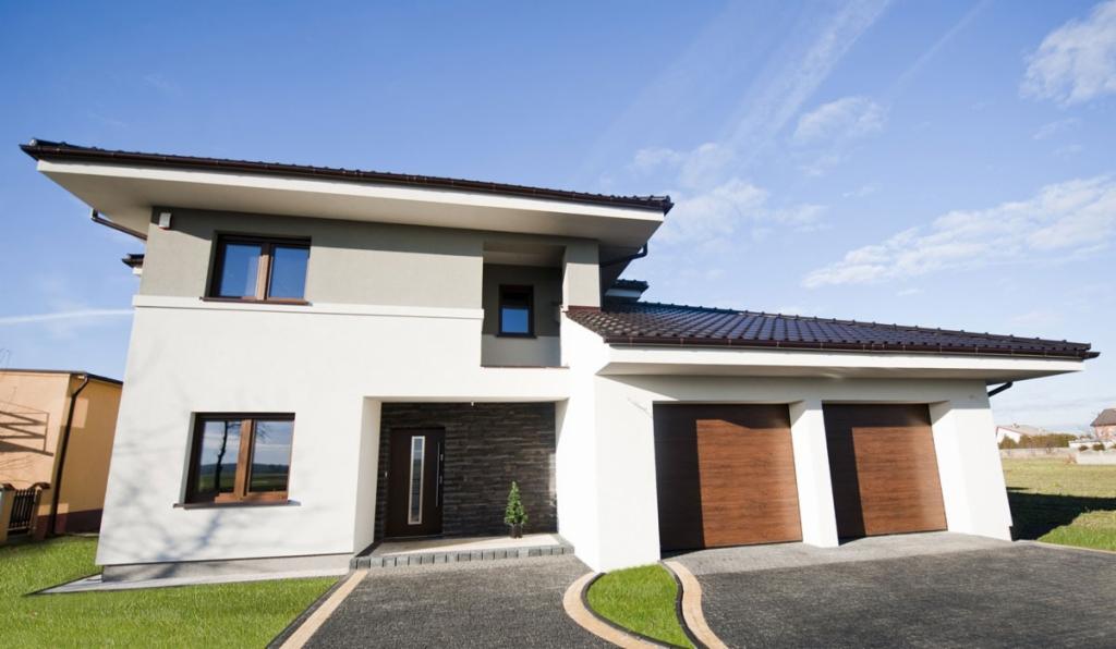 Nowoczesny dom jednorodzinny w Gorzowie Wielkopolskim z dwoma bramami garażowymi o drewnopodobnym wykończeniu, widoczne wejście z ciemną elewacją i małą choinką oraz podjazd z ciemnej kostki.