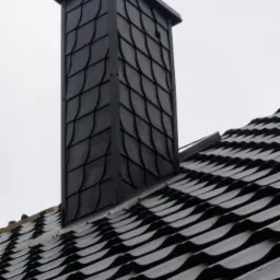 Czarny komin obłożony łupkiem na tle czarnego dachu z blachy trapezowej, widoczne połączenie komina z dachem.