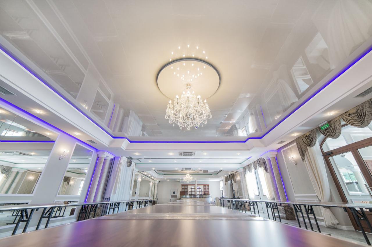 Sala konferencyjna z długim stołem, błyszczącym białym sufitem podwieszanym z oświetleniem LED, kryształowym żyrandolem i kolumnami dekoracyjnymi.