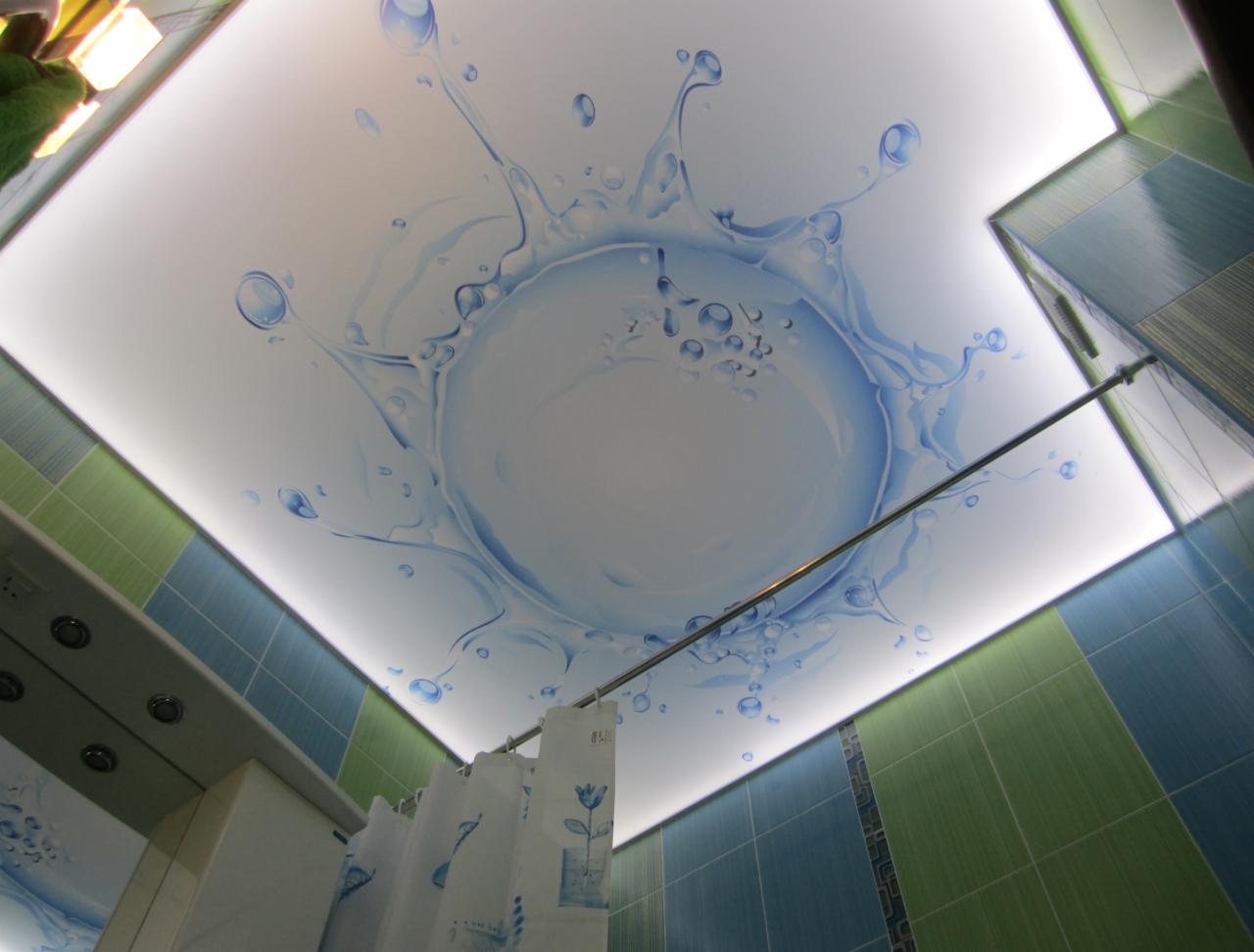 Podświetlany sufit napinany w łazience z nadrukiem błękitnych kropli wody i efektu rozprysku, widoczne niebiesko-zielone płytki i zasłonka prysznicowa.