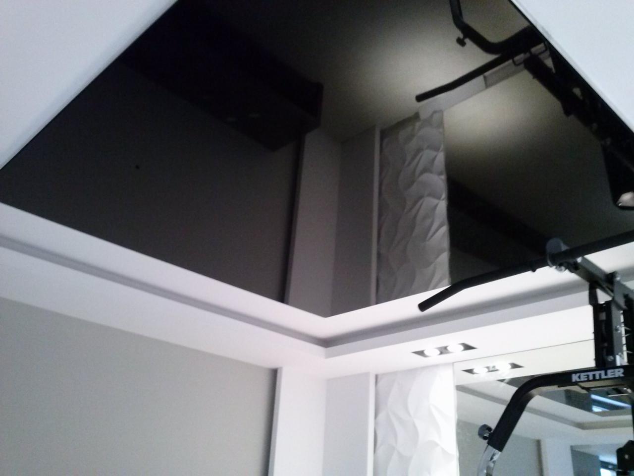 Czarne lustrzane odbicie sufitu w pomieszczeniu z białymi ścianami, dekoracyjnym panelem 3D i częścią sprzętu do ćwiczeń Kettler.
