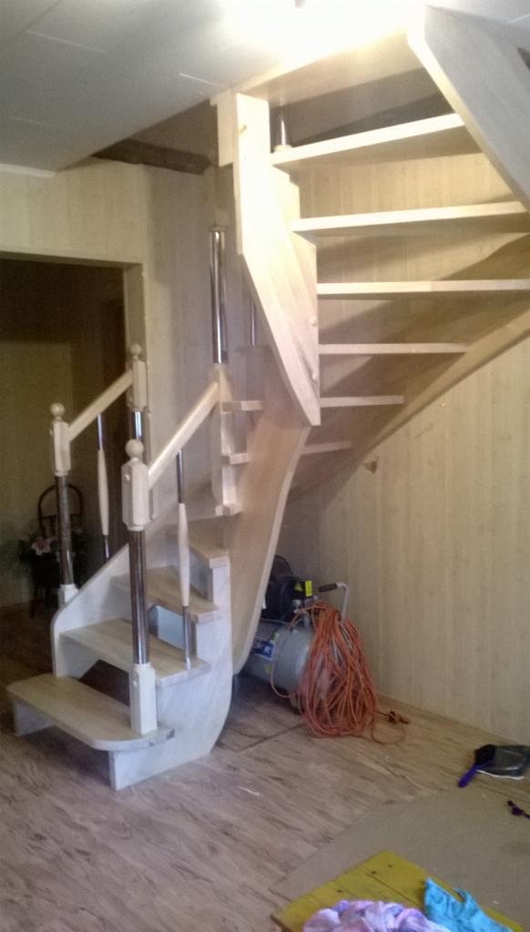 Drewniane schody spiralne z metalowymi balustradami w trakcie montażu, widoczny kompresor i narzędzia w tle.